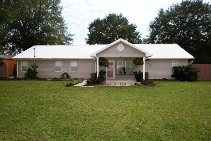 Single-story house with a front porch, garden, and green lawn.